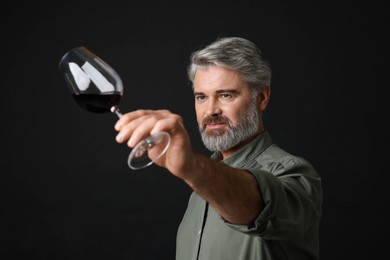 Photo of Professional sommelier analyzing quality of red wine on black background