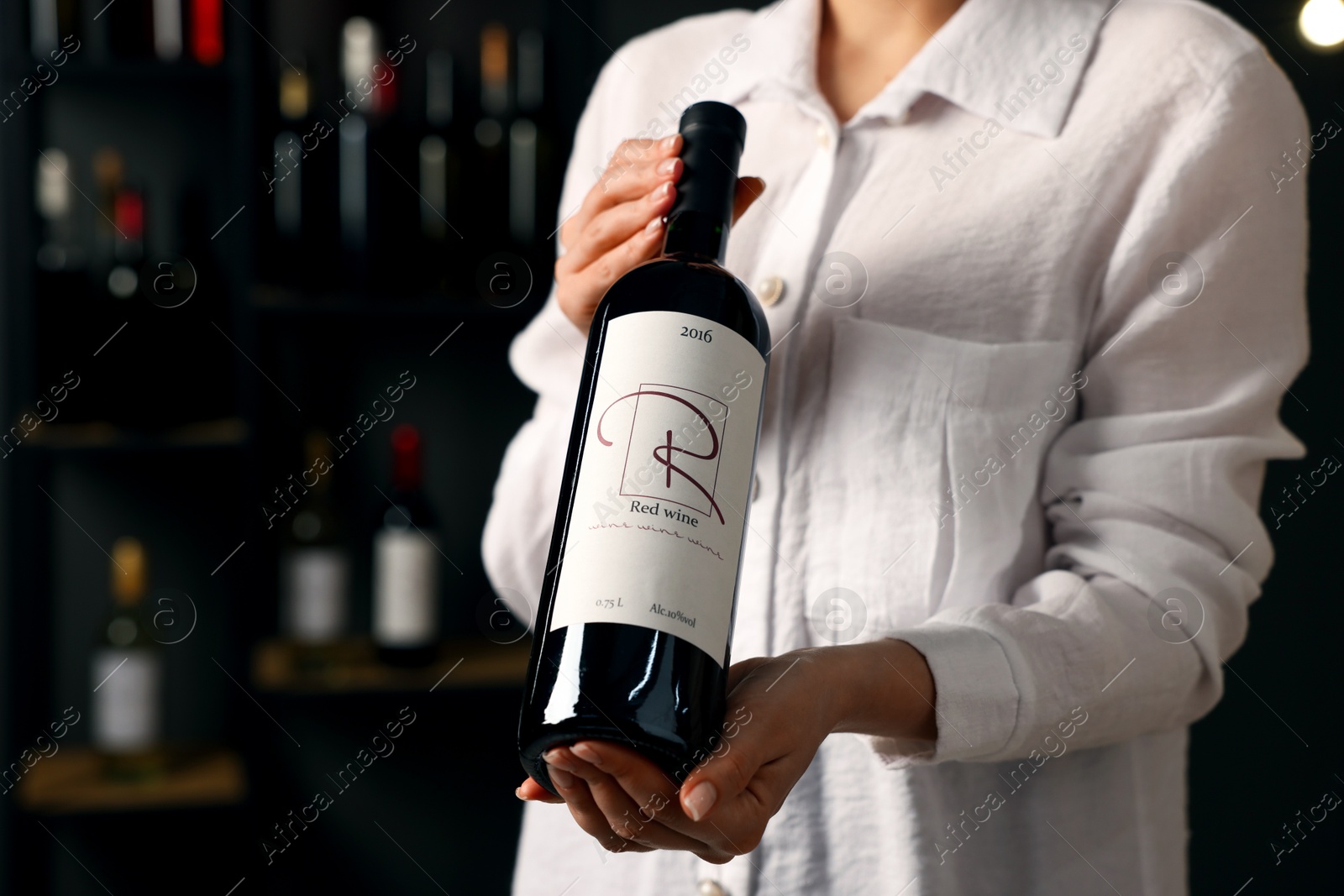 Photo of Professional sommelier holding bottle of red wine indoors, closeup. Space for text