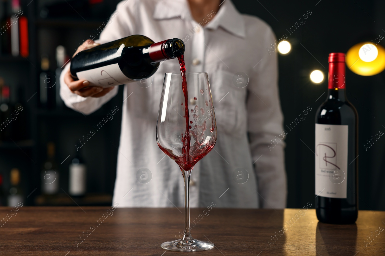 Photo of Professional sommelier pouring red wine into glass at wooden table indoors, closeup