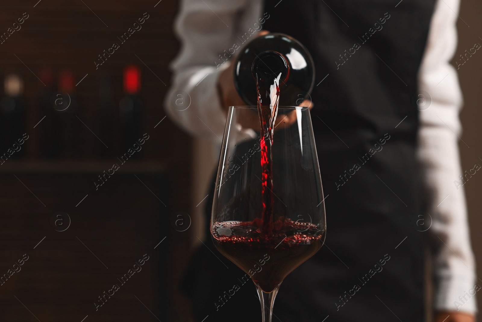 Photo of Professional sommelier pouring red wine into glass indoors, closeup