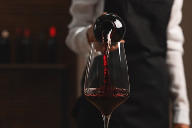 Photo of Professional sommelier pouring red wine into glass indoors, closeup