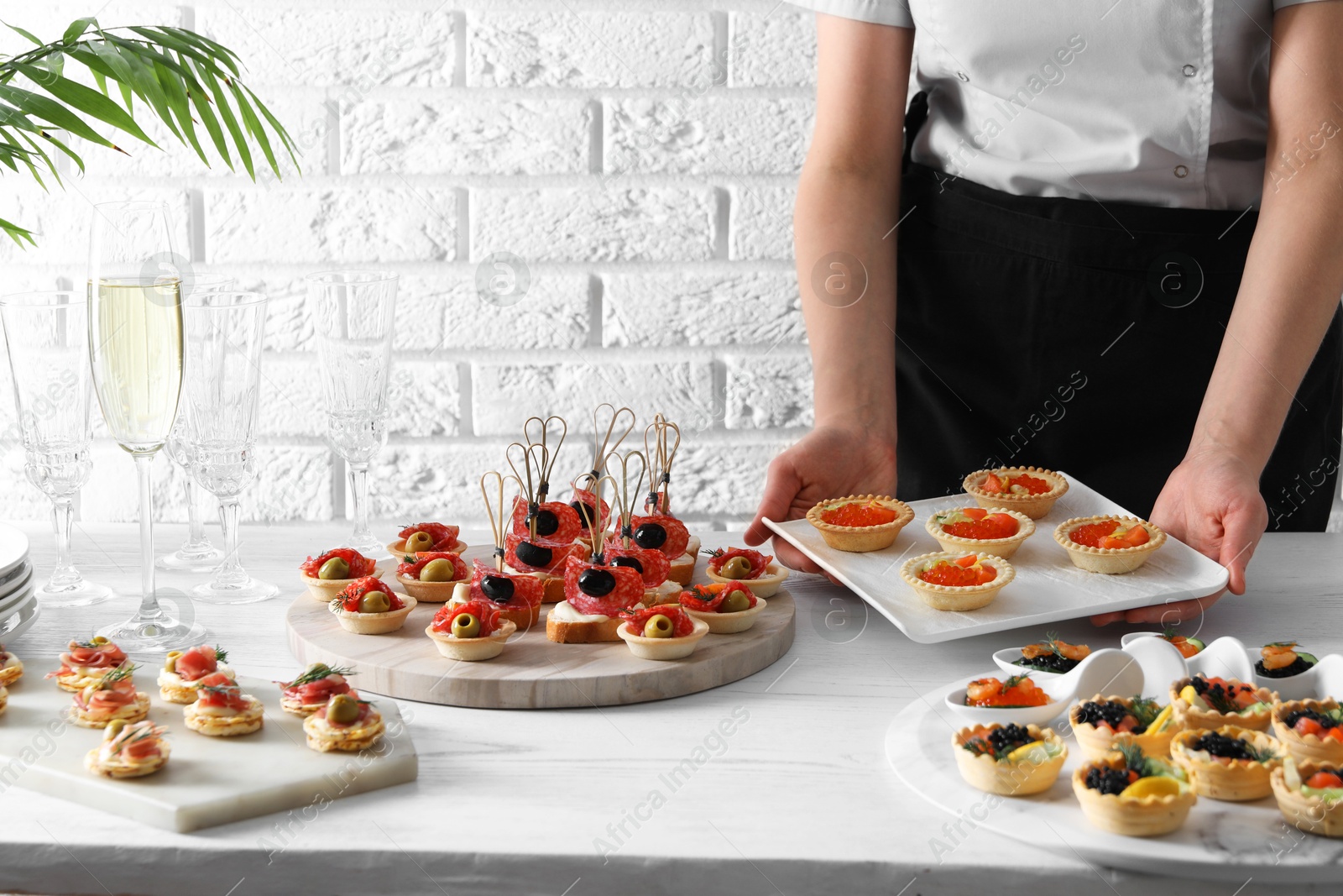 Photo of Woman with many different tasty canapes at white wooden table, closeup