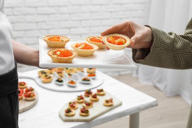 Photo of Woman taking tasty canape from waiter with board indoors, closeup