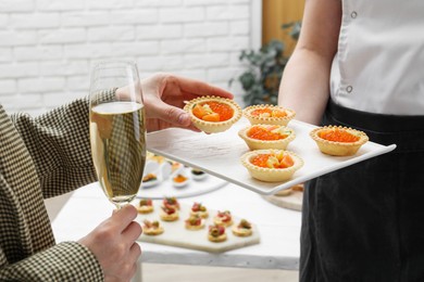 Photo of Woman taking tasty canape from waiter with board indoors, closeup