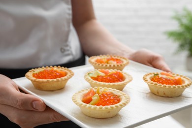 Photo of Woman holding board with tasty canapes indoors, closeup