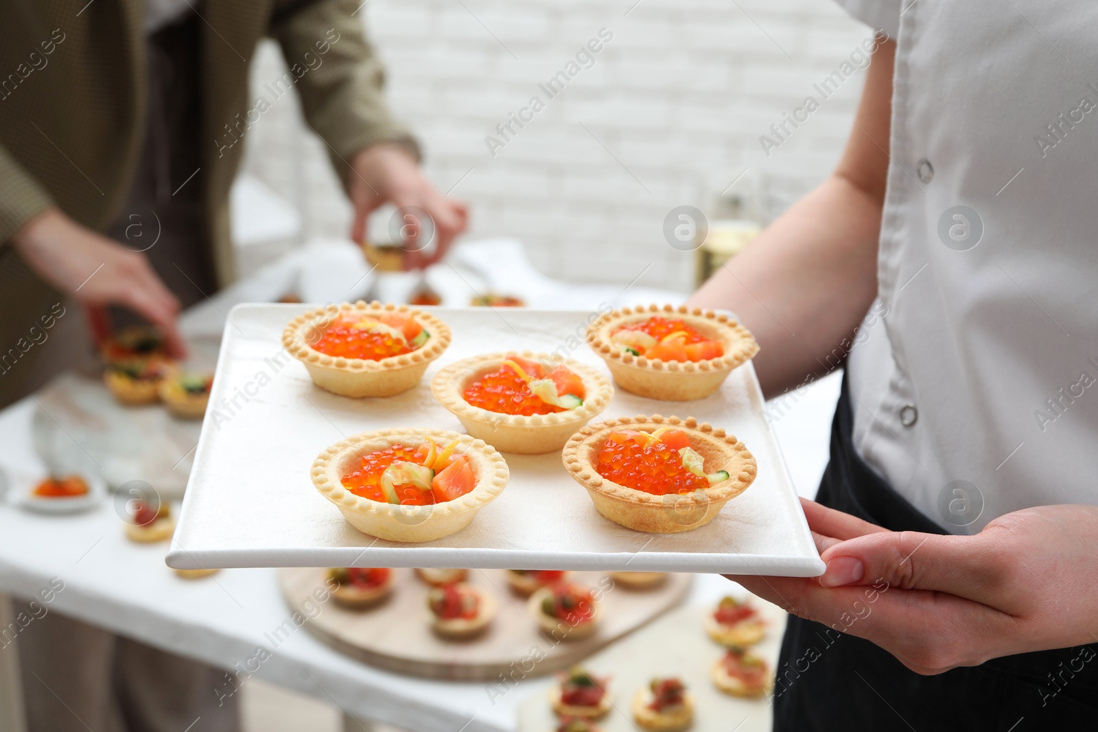 Photo of Woman holding board with tasty canapes indoors, closeup