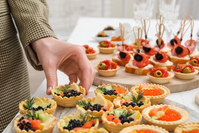 Photo of Woman taking tasty canape at white wooden table, closeup