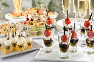 Photo of Many different tasty canapes and wine on white table, closeup