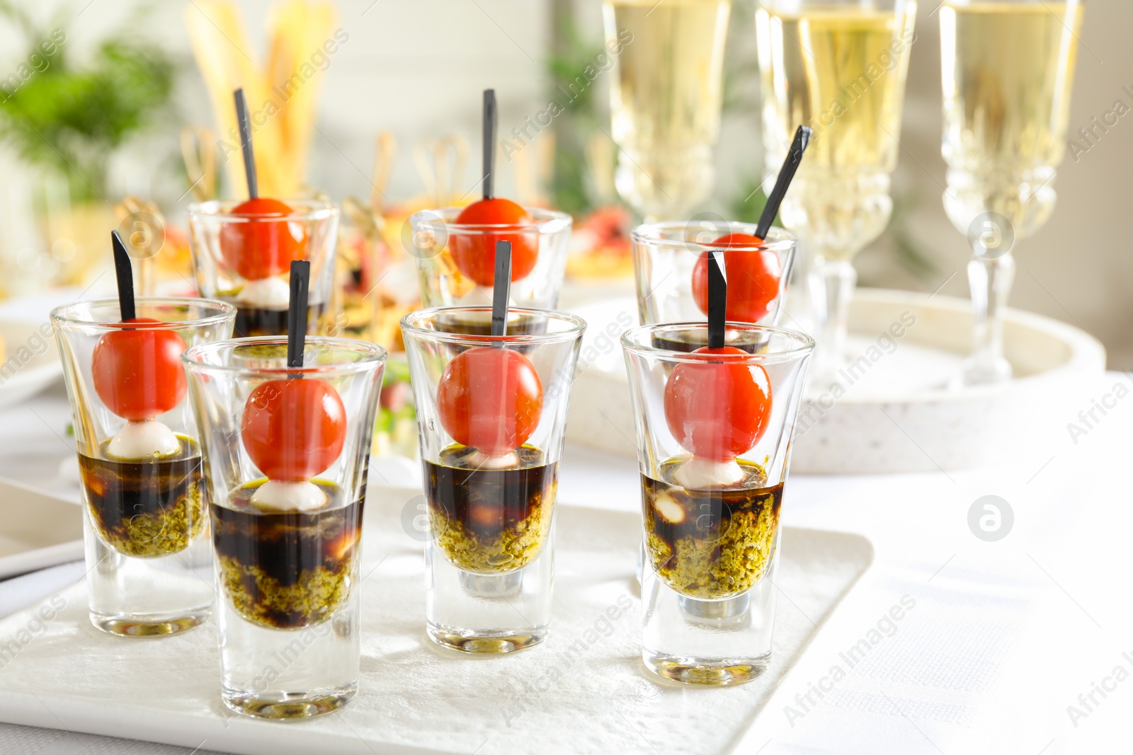 Photo of Tasty canapes with cherry tomatoes, mozzarella, balsamic vinegar and pesto sauce in shot glasses on white table, closeup