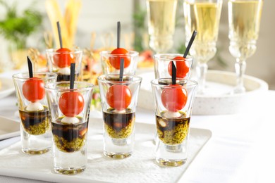 Photo of Tasty canapes with cherry tomatoes, mozzarella, balsamic vinegar and pesto sauce in shot glasses on white table, closeup