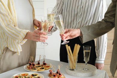 Photo of Many different tasty canapes on white table. People clinking glasses of wine indoors, closeup