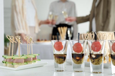 Photo of Many different tasty canapes on white table. People clinking glasses of wine indoors, closeup