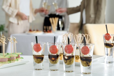 Photo of Many different tasty canapes on white table. People clinking glasses of wine indoors, closeup