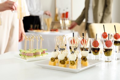 Photo of Many different tasty canapes on white table. People enjoying buffet meals indoors, closeup