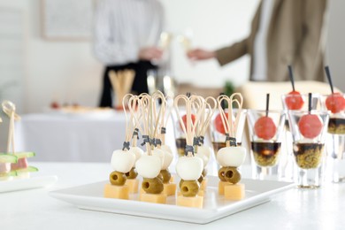 Photo of Many different tasty canapes on white table. People clinking glasses of wine indoors, closeup