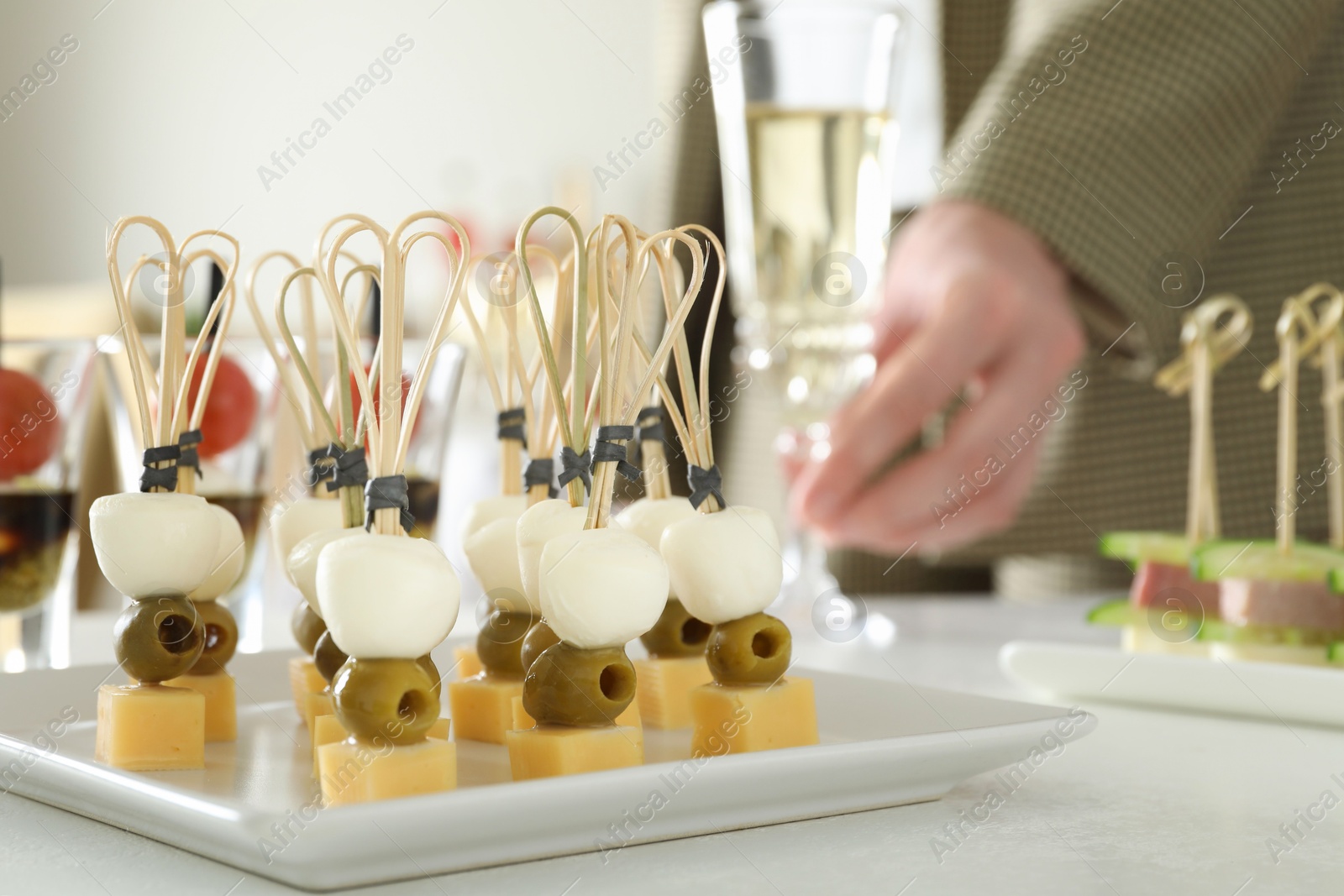 Photo of Many different tasty canapes on white table. Woman with glass of wine indoors, closeup