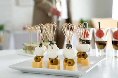 Photo of Many different tasty canapes on white table. Woman with glass of wine indoors, closeup