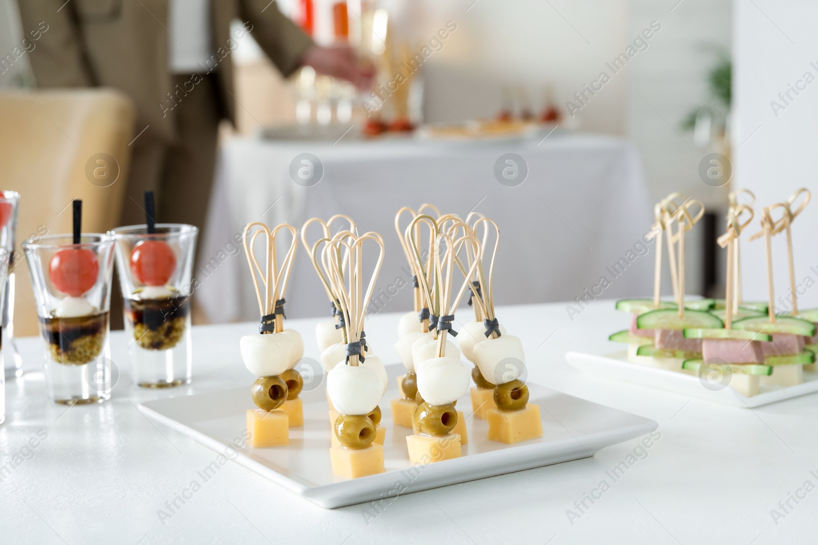 Photo of Many different tasty canapes on white table. Woman enjoying buffet meals indoors, closeup