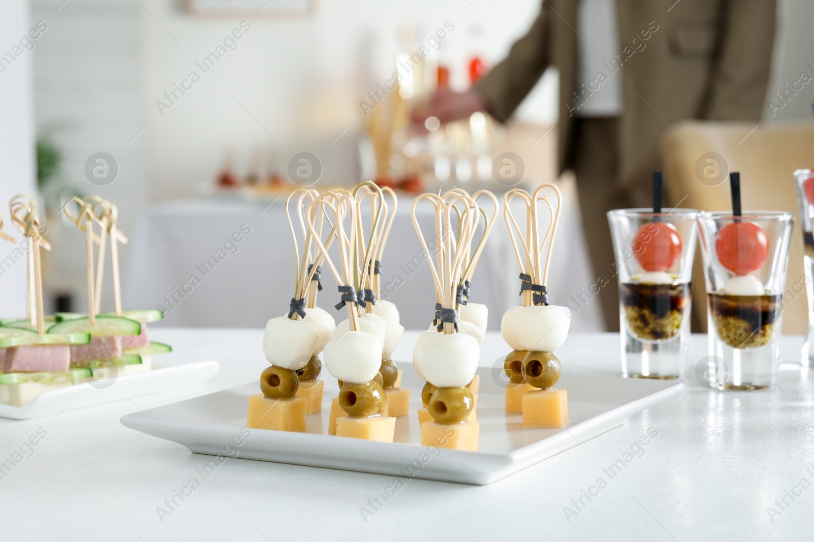 Photo of Many different tasty canapes on white table. Woman enjoying buffet meals indoors, closeup