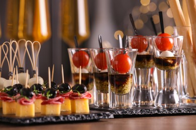 Photo of Many different tasty canapes and wine on wooden table against blurred lights