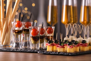 Photo of Many different tasty canapes and wine on wooden table against blurred lights