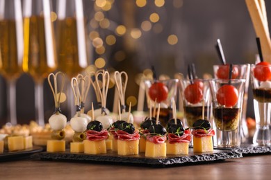 Photo of Many different tasty canapes and wine on wooden table against blurred lights