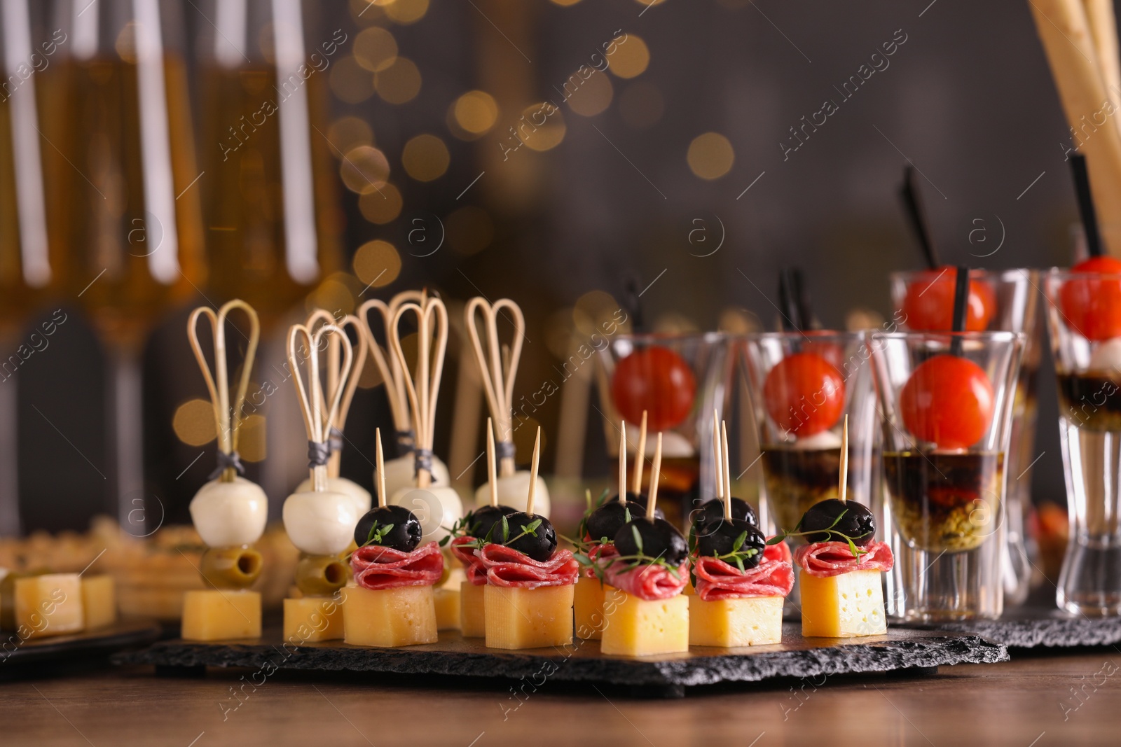 Photo of Many different tasty canapes on wooden table against blurred lights