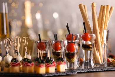 Photo of Many different tasty canapes on wooden table against blurred lights