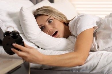 Photo of Overslept woman with alarm clock in bed at home