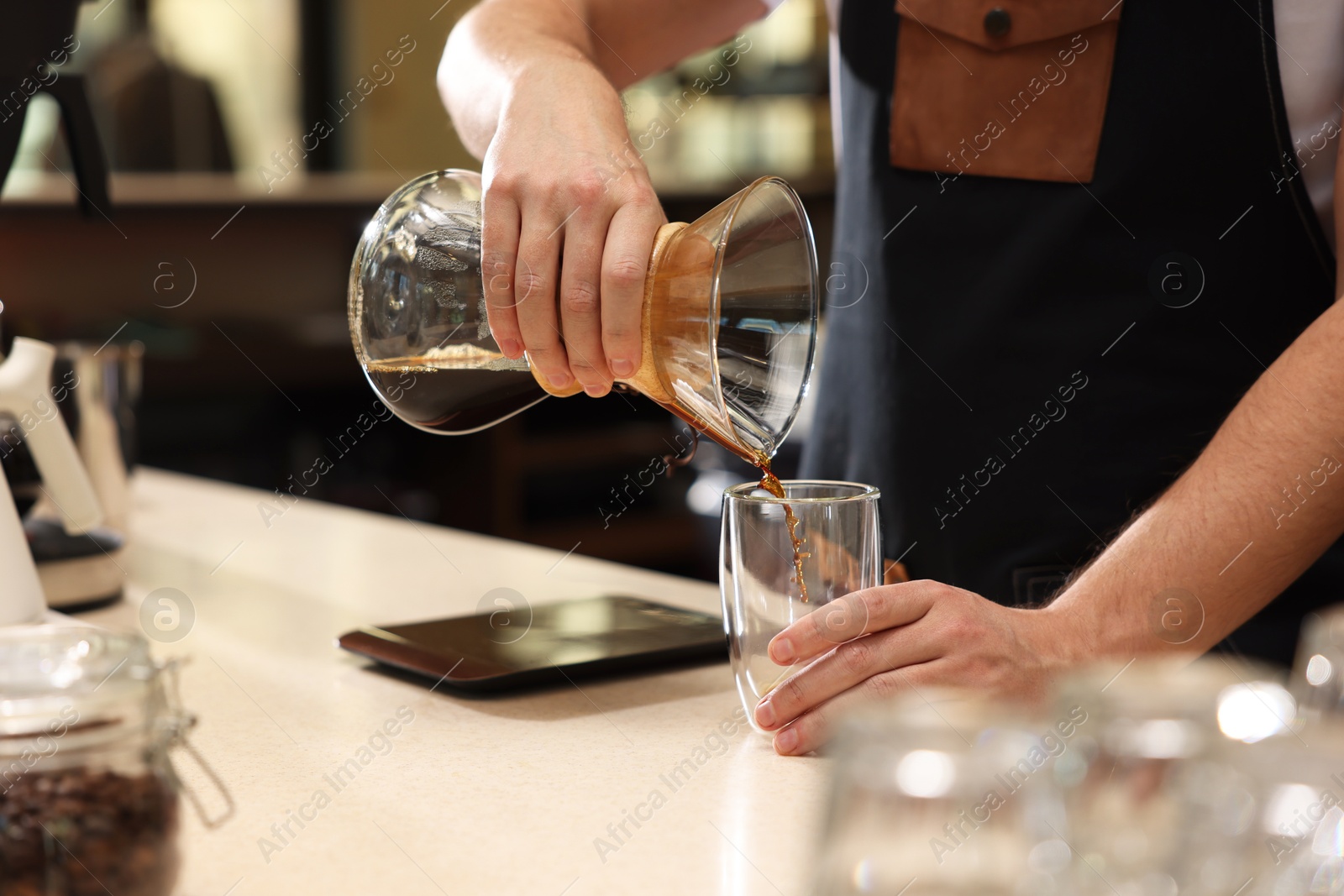 Photo of Barista pouring coffee from glass coffeemaker into cup at table in cafe, closeup