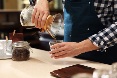 Photo of Barista pouring coffee from glass coffeemaker into cup at table in cafe, closeup