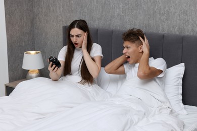 Photo of Shocked overslept couple looking at alarm clock in bed indoors