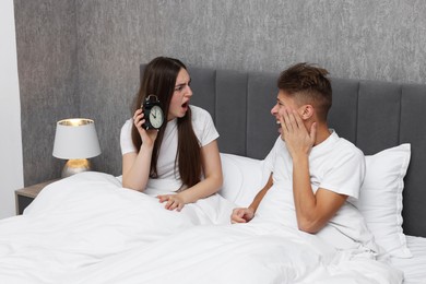 Shocked overslept couple looking at alarm clock in bed indoors