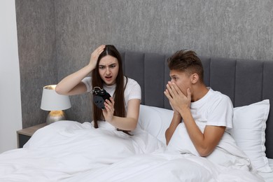 Shocked overslept couple looking at alarm clock in bed indoors