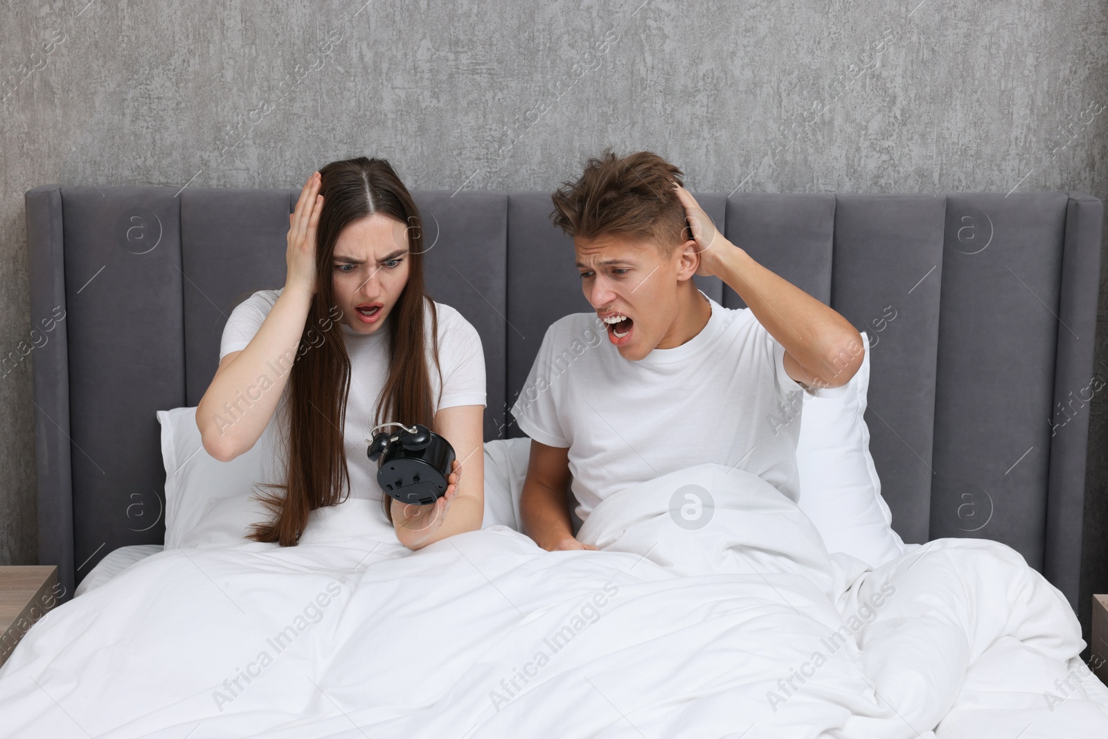 Photo of Shocked overslept couple looking at alarm clock in bed indoors