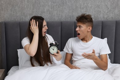 Shocked overslept couple with alarm clock in bed at home