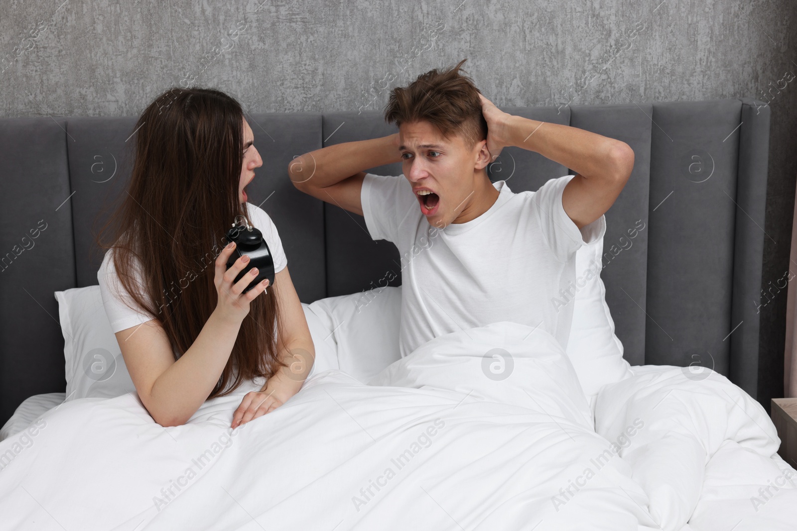 Photo of Shocked overslept couple looking at alarm clock in bed indoors