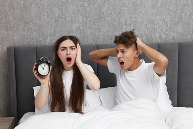 Shocked overslept couple with alarm clock in bed at home