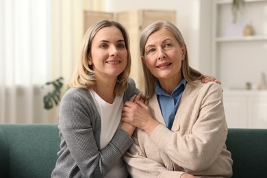 Photo of Smiling daughter and her mother on sofa at home