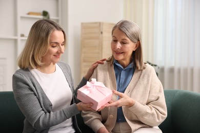 Photo of Smiling daughter congratulating her mom with gift on sofa at home. Happy Mother's Day