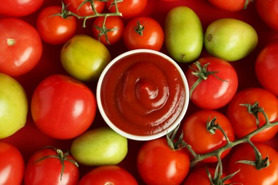 Photo of Ketchup in bowl and fresh tomatoes on red background, top view