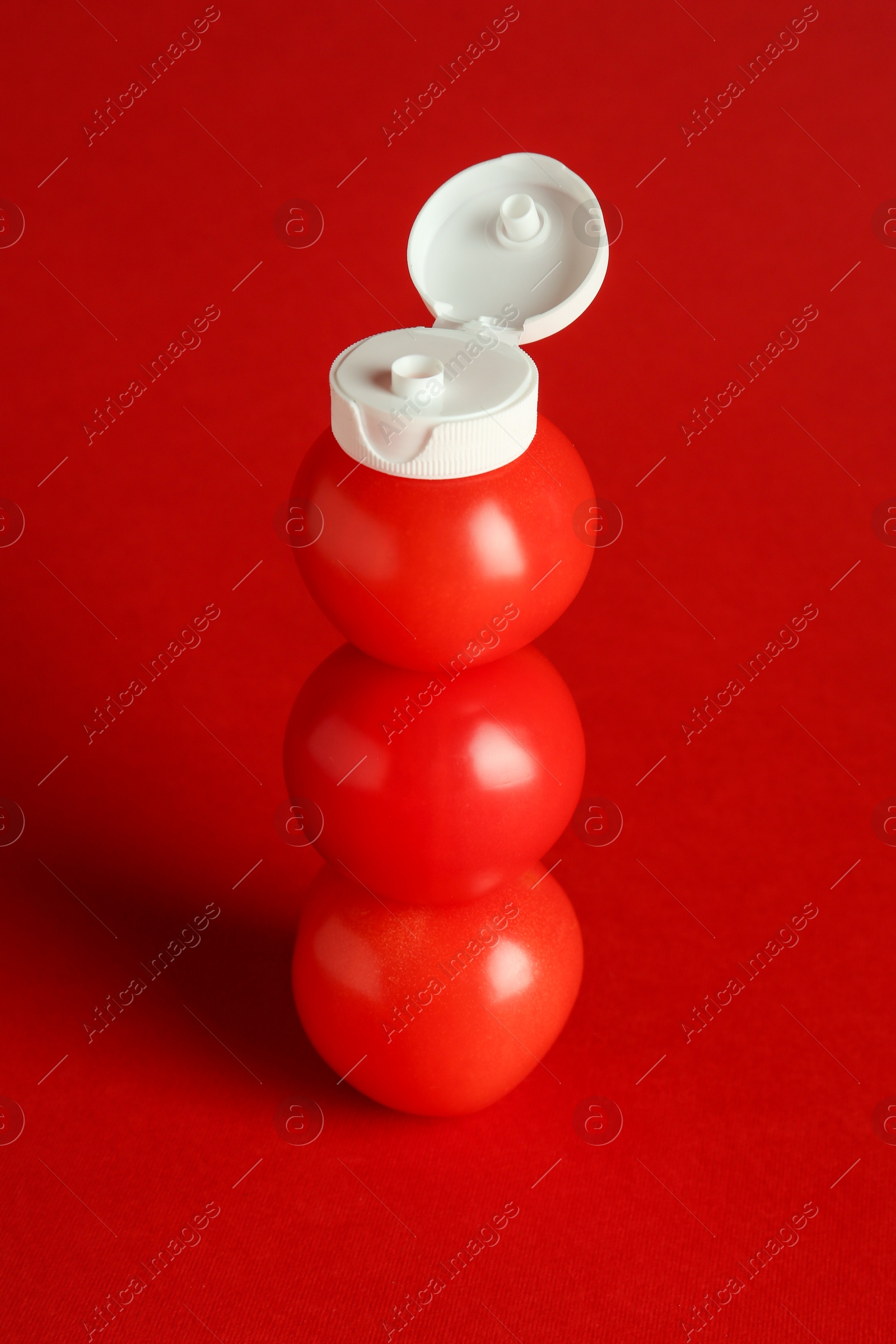 Photo of Stack of fresh tomatoes with plastic cap as bottle of ketchup on red background