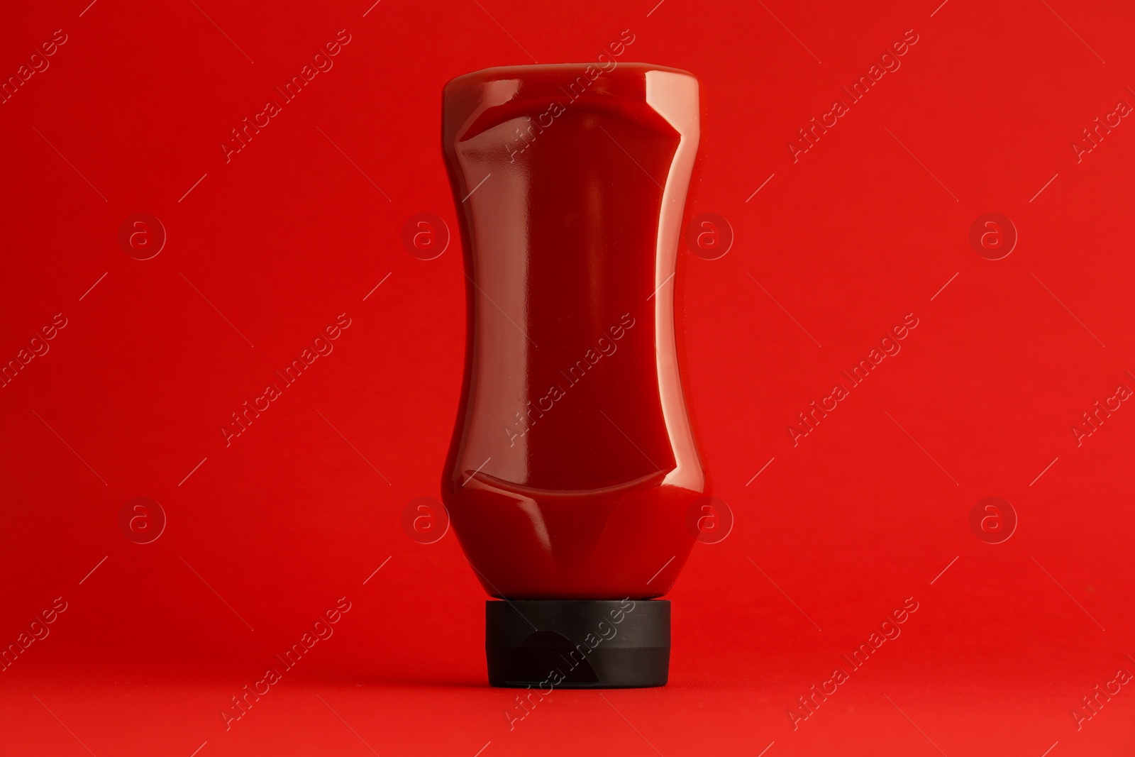 Photo of Ketchup in plastic bottle on red background