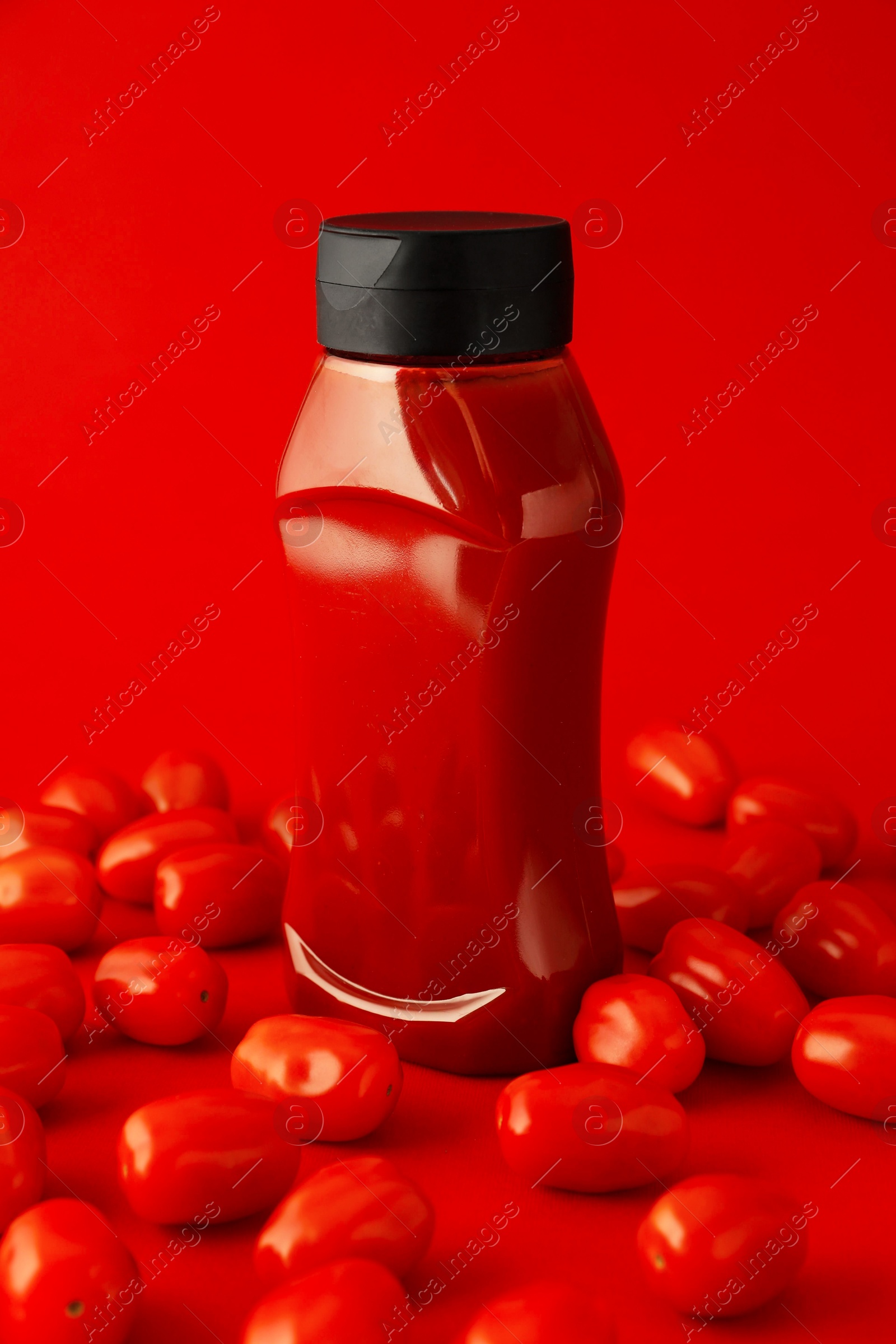 Photo of Bottle of ketchup and tomatoes on red background