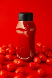 Photo of Bottle of ketchup and tomatoes on red background