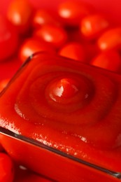 Photo of Ketchup in bowl and tomatoes on red background, closeup