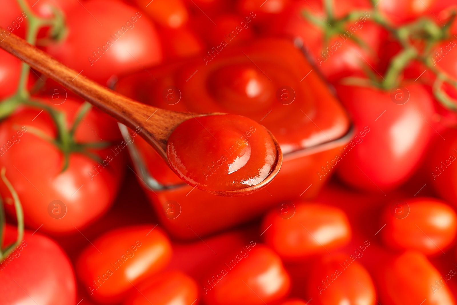 Photo of Spoon with delicious ketchup over tomatoes, closeup