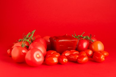 Photo of Ketchup in bowl and tomatoes on red background