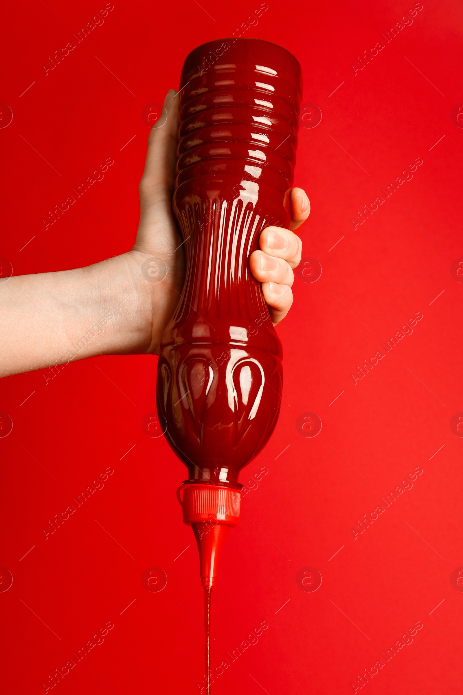 Photo of Woman squeezing ketchup out of bottle on red background, closeup