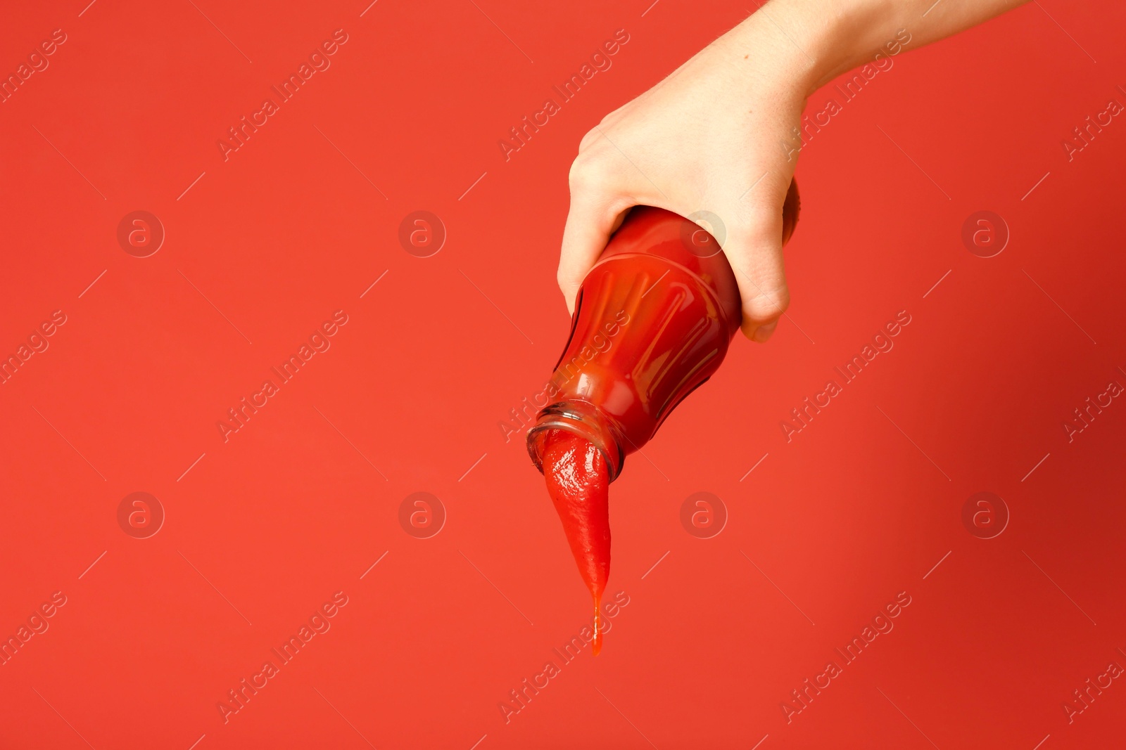 Photo of Woman pouring ketchup out of bottle on red background, closeup. Space for text